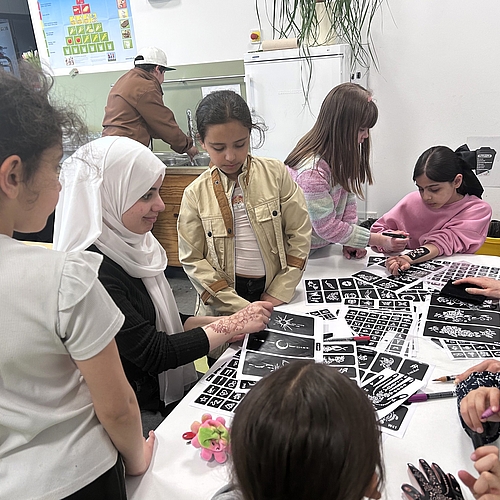 Kinder und Familien sitzen in einem Gemeinschaftsraum an mehreren Tischen, essen zusammen und unterhalten sich.
